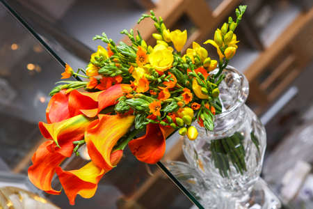 Colorful bouquet of orange calla lilies and other flowers in a clear vase on the table.の写真素材