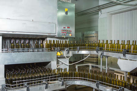 Unlabeled glass bottles in bottling machine at modern winery
