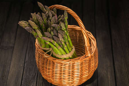 Bunch of fresh green asparagus spears in basket on a rustic wooden table.の写真素材