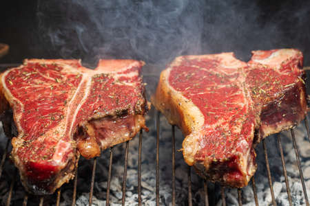 Selection of meat and vegetables grilling on a portable summer barbecue outdoors with focus to a succulent lean t-bone steak with rosemary seasoning in the foreground.の写真素材