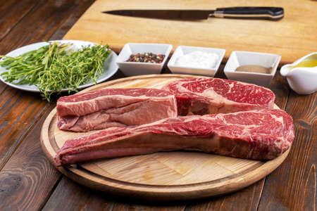 Raw tomahawk beef steak with ingredients for grilling with a spice rub, fresh rosemary and kitchen knife on blackの写真素材