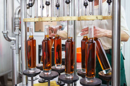 Unlabeled glass bottles in bottling machine at modern wineryの写真素材