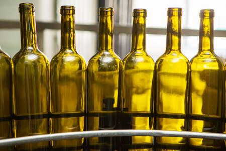 Unlabeled glass bottles in bottling machine at modern wineryの写真素材