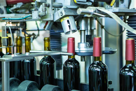 Unlabeled glass bottles in bottling machine at modern wineryの写真素材
