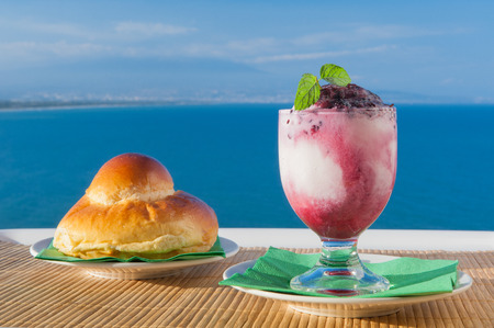 Glass of sicilian granita and a typical warm brioche with sea and mount etna in the backgroundの写真素材