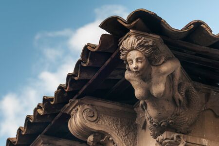 Sculpture of a mermaid used as architectural element under a tile roof of an old baroque palaceのeditorial素材