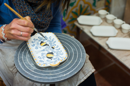 Pottery decorator from Caltagirone while finishing a ceramic dish in her work spaceの写真素材