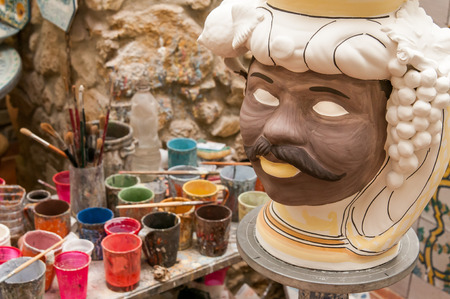 Ceramic head of an arab man in the studio of a decorating artisan in Caltagirone and glasses for colors in the backgroundの写真素材