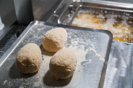 three typical sicilian arancini placed on an iron tray before being fried and a deep fryer in the backgroundの写真素材