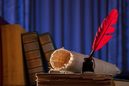 Red quill pen, black inkwell and a rolled papyrus sheet on an old book with a blue backgroundの写真素材