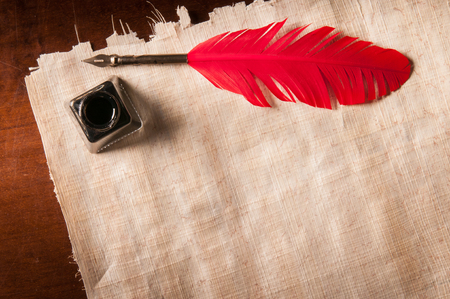 Red quill pen and black inkwell on a papyrus sheetの写真素材