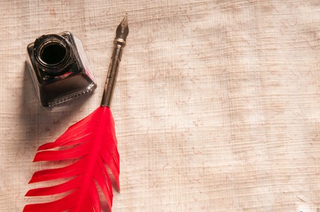 Red quill pen and black inkwell on a papyrus sheetの写真素材