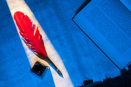 Red quill pen and black inkwell on a papyrus sheet surrounded by a blue lightの写真素材