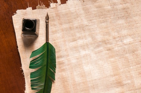 Green quill pen and black inkwell on a papyrus sheetの写真素材