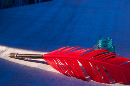 Red quill pen and black inkwell on a papyrus sheet enlightened by a beam of light
