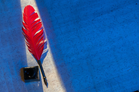 Red quill pen and black inkwell on a papyrus sheet enlightened by a beam of lightの写真素材