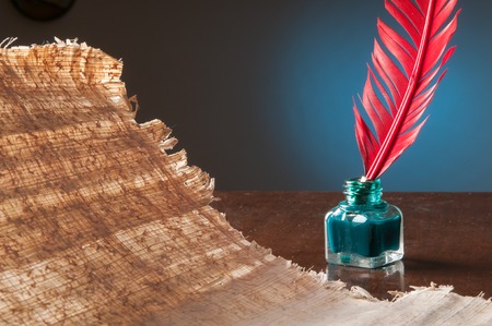 Red quill pen and a papyrus sheet on a wooden table in a blue backgroundの写真素材
