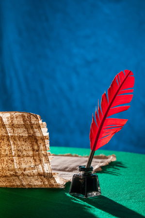 Red quill pen and a papyrus sheet on a green table and with a blue backgroundの写真素材