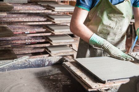 Artisan flattening the clay inside a mold to make square terracotta tiles