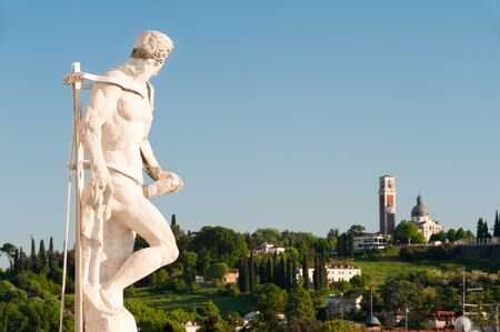 Ornamental white stone statue on the top of the Palladian basilica in Vicenza and Mount Berico in the backgroundの写真素材