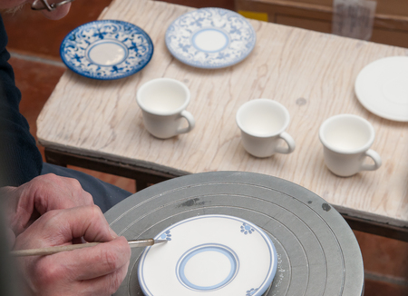 Ceramic artist in Caltagirone, Sicily, decorating some coffee saucers in his workshopの写真素材