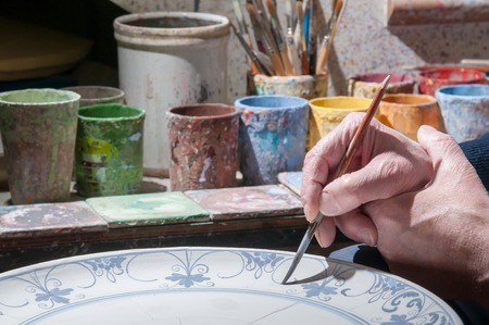 Ceramic artist in Caltagirone, Sicily, decorating a ceramic dish in his workshopの写真素材