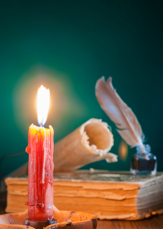 Closeup view of a candle with a quill pen and an old book in the backgroundの写真素材