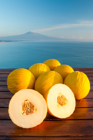 Open yellow melon of West Siciiy on a wooden table with blue sea and Mount Etna in the backgroundの写真素材