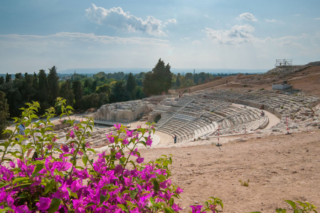 The famous greek theater of Syracuse, Sicily, with a flowered bougainvillae plant in the foregroundの写真素材