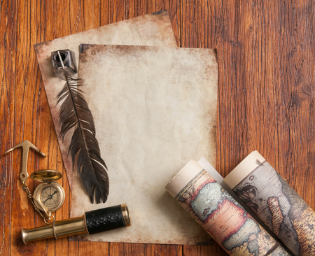 Quill pen on old paper sheets with old rolled maps and vintage items