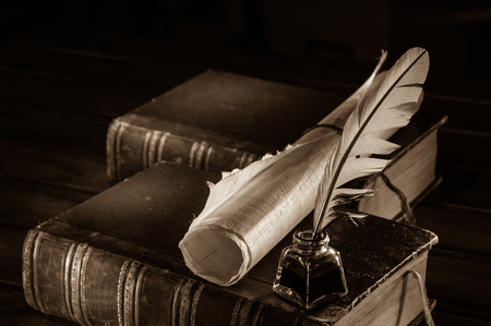 Quill pen and a rolled papyrus sheet on old books, sepia effectの写真素材