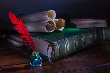 Quill pen and a rolled papyrus sheet on a wooden table with old books