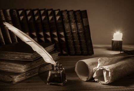 Quill pen and a rolled papyrus sheets with old books at candle light, sepia effect