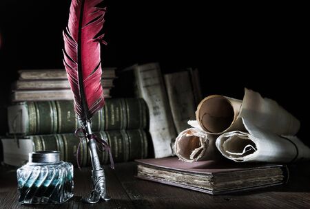 Quill pen and rolled papyrus sheets on a wooden table with old books, high contrast
