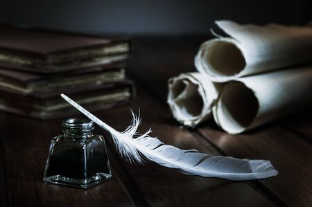 Quill pen and rolled papyrus sheets on a wooden table with old books, high contrastの写真素材