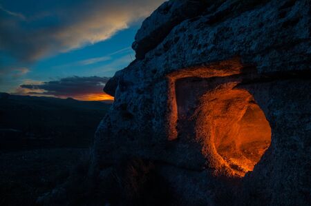 View of a rock-cut tomb in the rocky necropolis of Pantalica enlightened from behind at the dusk