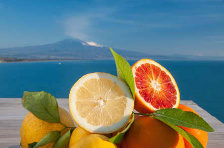 Cut oranges and lemons on a wooden table with blue sea and Mount Etna in the backgroundの写真素材