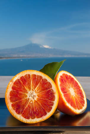 Cut oranges on a wooden table with blue sea and Mount Etna in the backgroundの写真素材