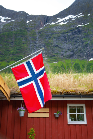 Flag of Norway against the background of the national Norwegian house of red color, on the roof of which grass grows. Flag of Norway, national symbol with nature in the background.の写真素材