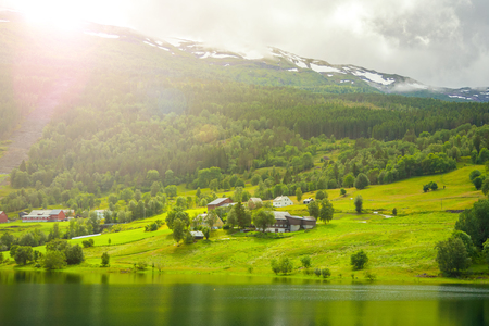 Village is located on the green slopes near lake. Scenic summer view of cottage houses in mountain village near lake, Norway. Tourism holidays and travel.の写真素材