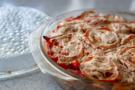 Baked tomatoes with vegetables. Freshly baked home made mix of vegetables. Close-up of vegetable dish with baked tomatoes. Homemade vegetable dish in a glass bowl on a gray countertop, closeup.の写真素材