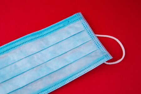 Medical mask. Medical protective masks on red background. Disposable surgical face mask cover the mouth and nose. Healthcare and medical concept. Blue medical disposable face mask, close up on red.の写真素材