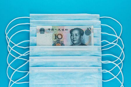 10 yuan bill in a stack of medical masks. The rise in price of medical masks. COVID-19 coronavirus in China. Shortage of face masks. Blue medical masks, and money. Top view, close-upの写真素材