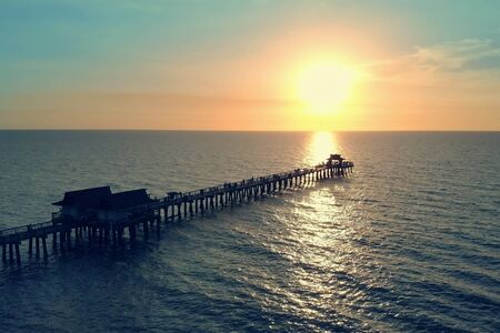 Naples Beach and Fishing Pier at Sunset, Florida. Dark silhouette of a pier over the water at sunset. Sunset over horizon and wooden pier of caribbean beach of Naples in Florida. Sunset over the Pier.の写真素材