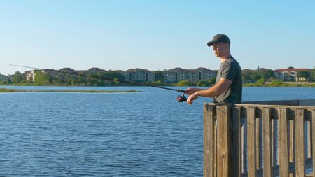 Fisherman throws a fishing tackle into the lake from a wooden pier.の写真素材