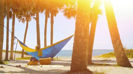 Romantic couple relaxing on tropical hammock. Young couple in love relaxing in a hammock by the beach. Summer luxury vacation. Lens Optical Flare. Vintage Overlay Effect.の写真素材