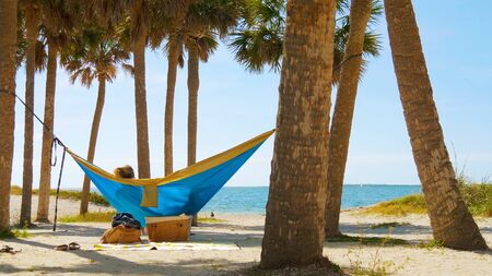 Romantic couple relaxing on tropical hammock. Young man and girl in blue hammock from back in beautiful beach. Young couple in love relaxing in a hammock by the beach. Summer luxury vacation.の写真素材