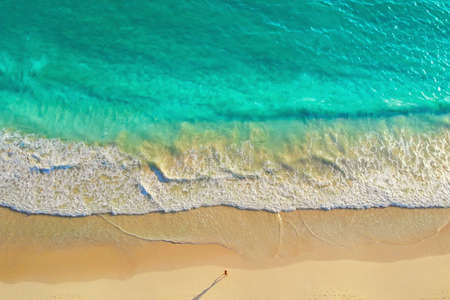Man running along the ocean coast, top view. Overhead view of man run by the white sandy beach along the amazing clear light blue ocean. Run along the coast of the ocean at sunrise. Healthy lifestyle.の写真素材