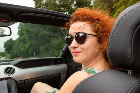 Portrait of beautiful young woman in sunglasses sitting in luxury modern cabriolet car. Portrait happy woman in convertible. travel, road trip and people concept - happy young woman in convertible carの写真素材