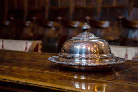 Silver bowl for serving hot dishes stands on a wooden oak table in a vintage interior. Silver vintage crockery close-up against a blurred background.の写真素材